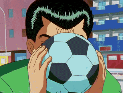 a man in a green shirt holds a soccer ball in front of his face
