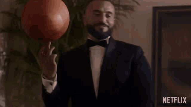 a man in a tuxedo and bow tie is holding a basketball in his hand .