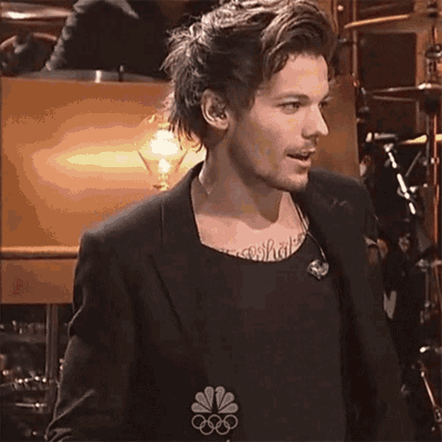 a man with a tattoo on his chest is wearing a black jacket and a black tank top .