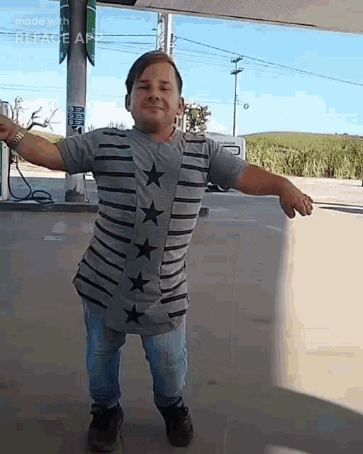 a man in a striped shirt with stars on it is standing in a parking lot with his arms outstretched