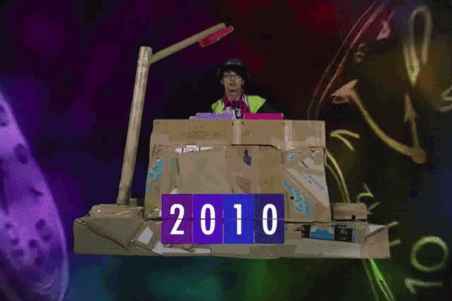 a man in a yellow vest stands behind a pile of cardboard boxes with 2010 written on them