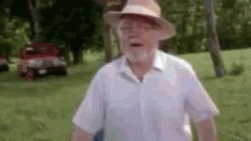 an older man wearing a hat and a white shirt is standing in a field .