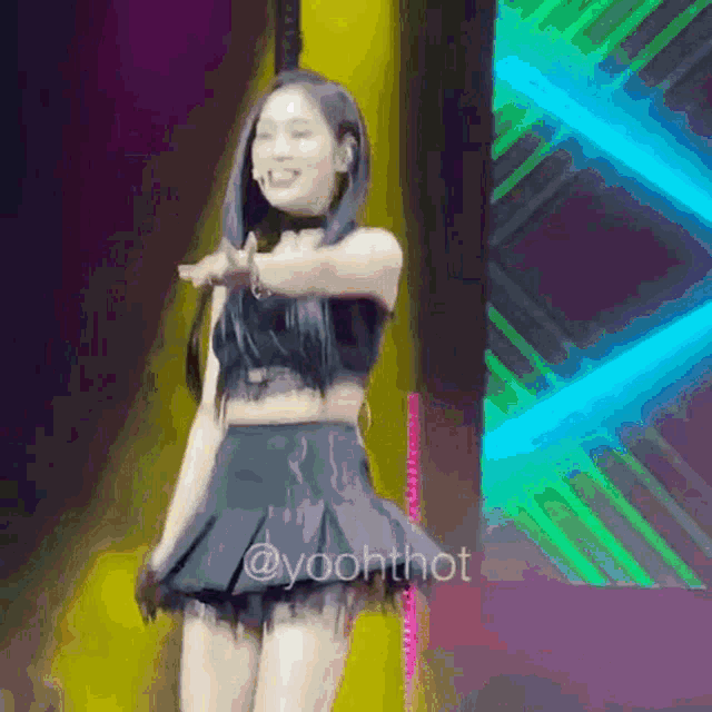 a woman in a crop top and skirt is dancing on a stage in front of a colorful background .