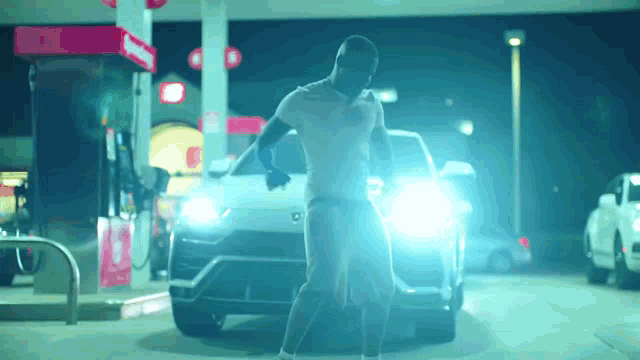 a man is standing in front of a car at a gas station at night