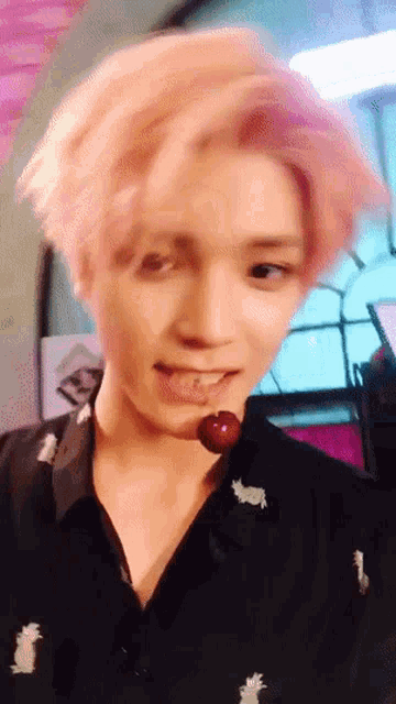 a young man with pink hair is biting a cherry