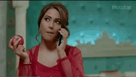 a woman is talking on a cell phone while holding an apple .