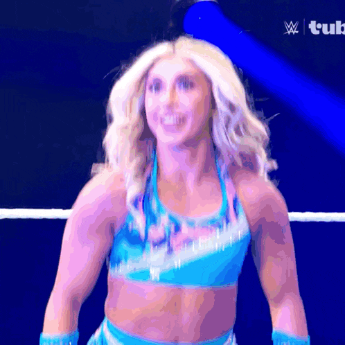 a woman in a blue top is standing in a wrestling ring with a w logo in the corner