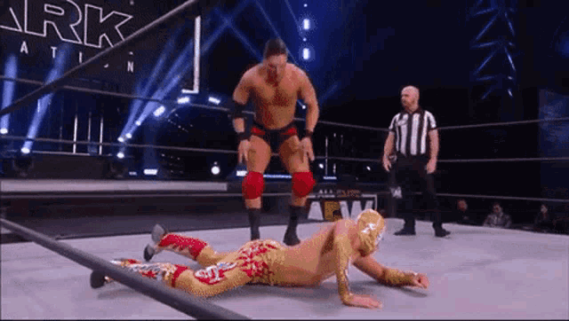 two wrestlers are wrestling in a ring while a referee looks on .