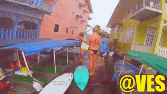 a woman in a bikini is carrying a surfboard in front of a building with the words @ves written on it