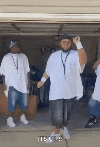a group of men are dancing in a garage and one of them is wearing a hat .