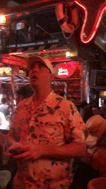 a man in a hawaiian shirt is standing in front of a sign that says ' a ' on it