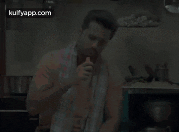 a man is sitting in a kitchen with a towel around his neck and eating a piece of food .