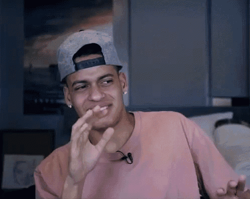 a man wearing a baseball cap and a pink shirt is making a funny face