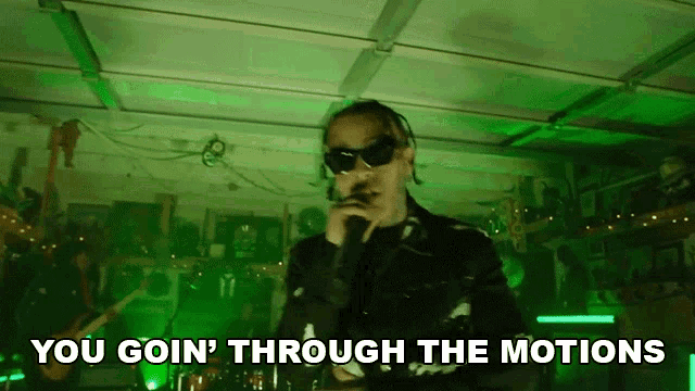 a man is singing into a microphone in a garage with the words `` you goin ' through the motions '' above him .
