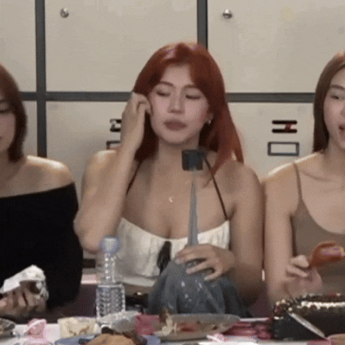 a woman with red hair is sitting at a table with two other women and a bottle of water