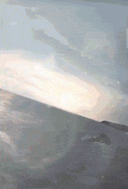 a plane is flying over a body of water and the sun is shining through the window