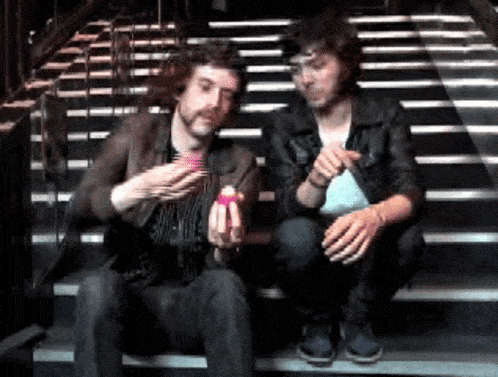two men are sitting on a set of stairs one is holding a pink object in his hand
