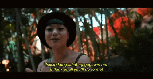 a woman wearing a black hat is standing in the woods with a quote on the screen .