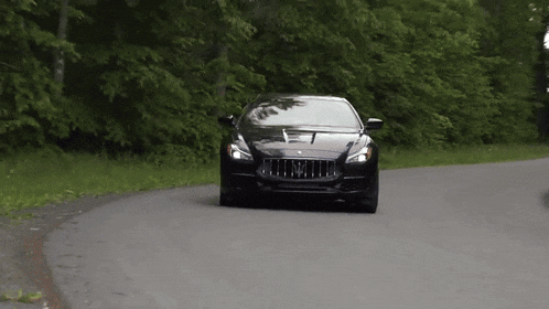 a black car with the letter m on the front is driving down a road