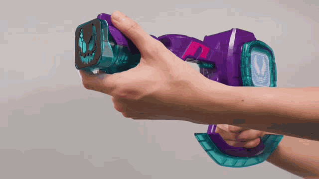 a person is holding a purple and blue toy gun in their hand .