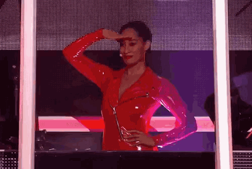 a woman in a red latex outfit is standing in front of a purple screen .