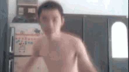 a shirtless man is jumping in front of a refrigerator in a kitchen .