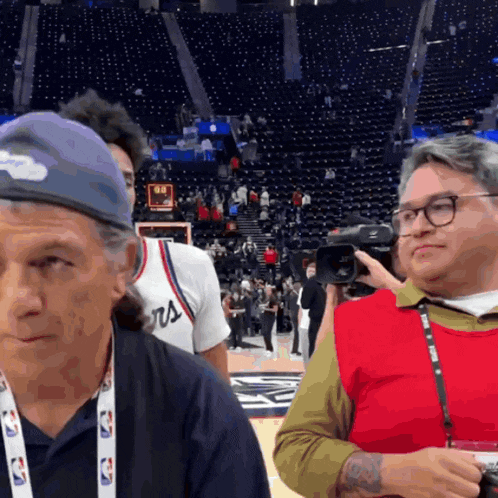 a man wearing a nba lanyard stands in front of a basketball court
