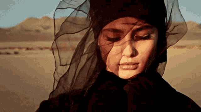a woman wearing a black veil on her head is standing in the desert .