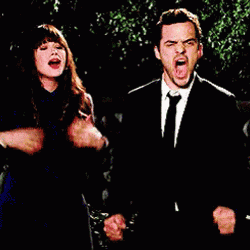 a man and a woman are standing next to each other with their fists in the air and screaming .