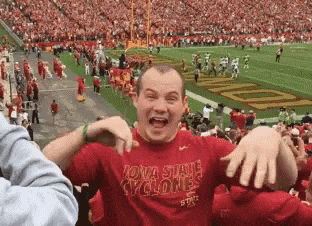 a man wearing a red shirt that says iowa state cyclones is standing in front of a football field