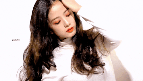 a woman with long hair is wearing a white turtleneck and has her hand on her forehead .