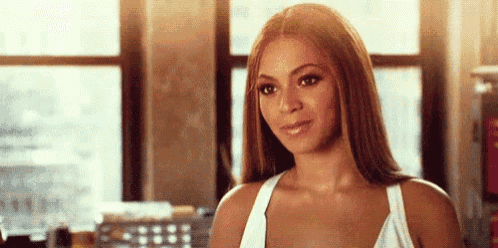 a woman in a white tank top is smiling and looking at the camera in front of a window .
