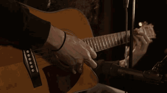 a man is playing an acoustic guitar in front of a microphone in a dark room