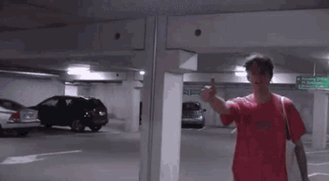 a woman in a red shirt is standing in a parking garage pointing at a green sign