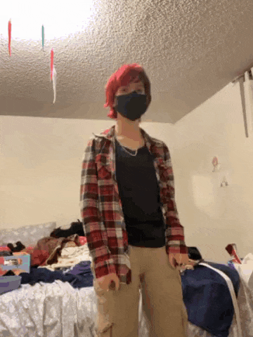 a person wearing a plaid shirt and a black mask is standing in a bedroom .