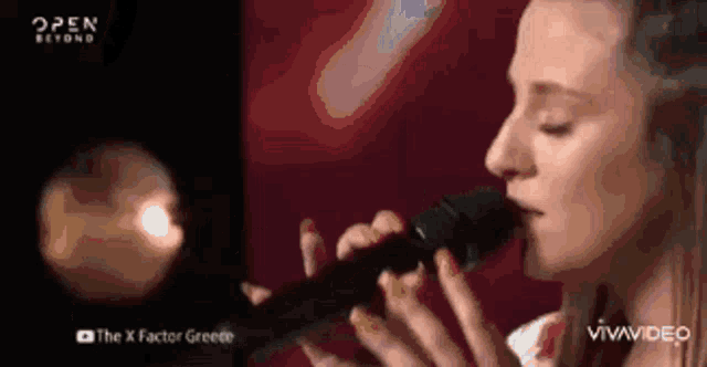 a woman is singing into a microphone with the x factor greece written on the bottom