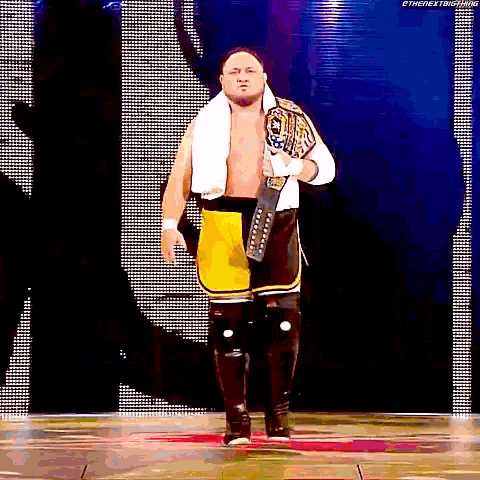a wrestler is walking down the aisle with a championship belt around his waist .