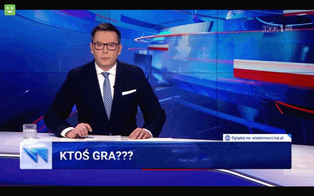 a man in a suit and tie is sitting at a desk with a sign that says ktos gra