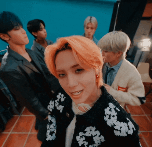 a group of young men are standing in a room and one of them has orange hair