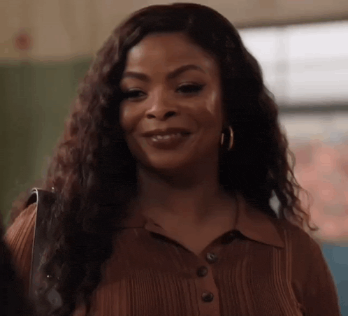 a woman wearing a brown shirt and earrings is smiling and looking at the camera .