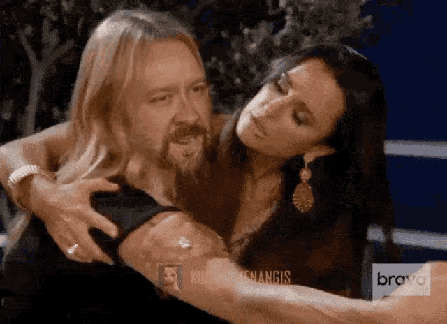 a man with long hair and a beard is being held by a woman with the word bravo on the bottom
