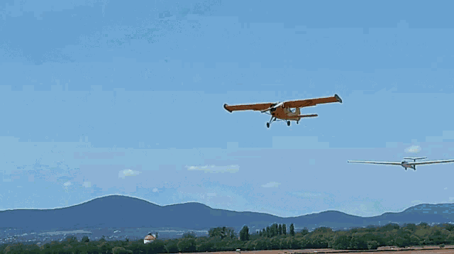 a small plane flies over a field with mountains in the background