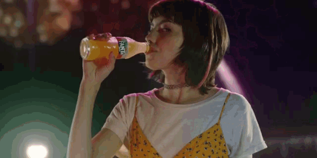 a woman is drinking from a bottle of fanta soda .