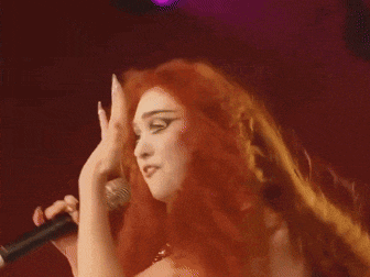 a woman with red hair singing into a microphone with her hand up