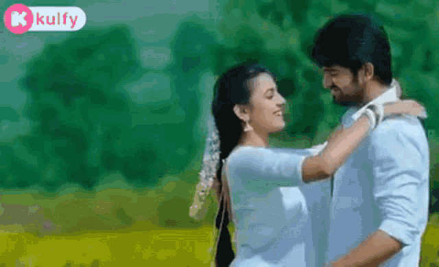 a man and a woman are standing next to each other in a field and hugging .