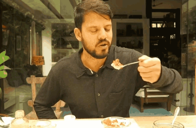 a man with a beard is eating food from a bowl with a spoon