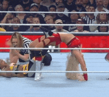 a woman in a red top is doing a handstand in a wrestling ring while a referee looks on