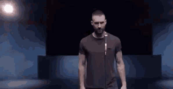 a man in a black t-shirt is standing in front of a microphone in a dark room .
