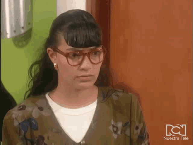 a woman wearing glasses stands in front of a door with nuestra tele written on the bottom