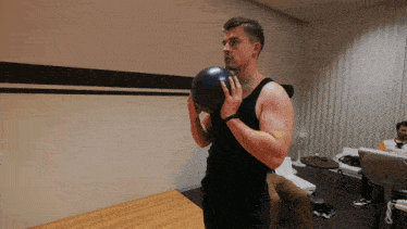 a man in a black tank top is holding a bowling ball in his right hand